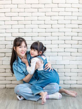 Mutlu Asyalı genç anne ve tatlı kız gülümseyen küçük kız beyaz tuğla duvar arkasında poz veren stüdyo resmi Anneler Günü aile babalığı kavramını seviyor..