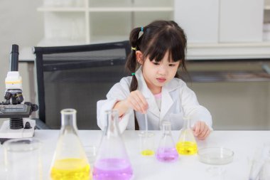 Laboratuvar önlüğü giymiş Asyalı küçük şirin kız öğrenciler deney tüpü bilim deneyleri yapıyorlar. Okulda kimya laboratuvarında. Eğitim araştırma ve geliştirme kavramı çocukları eğitiyor.