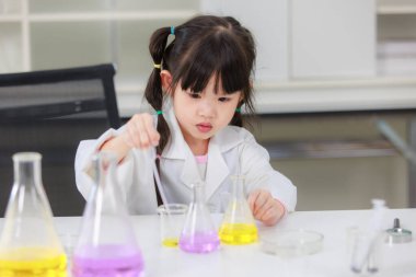 Laboratuvar önlüklü Asyalı küçük şirin kız öğrenciler, deney tüpü bilimi deneyleri yapmayı düşünüyorlar. Okulda kimya laboratuvarında. Eğitim araştırma ve geliştirme kavramı çocukları eğitiyor.