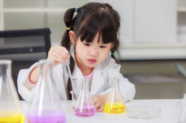 Laboratuvar önlüklü Asyalı küçük şirin kız öğrenciler, deney tüpü bilimi deneyleri yapmayı düşünüyorlar. Okulda kimya laboratuvarında. Eğitim araştırma ve geliştirme kavramı çocukları eğitiyor.