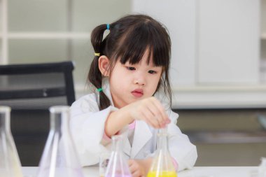 Laboratuvar önlüklü Asyalı küçük şirin kız öğrenciler, deney tüpü bilimi deneyleri yapmayı düşünüyorlar. Okulda kimya laboratuvarında. Eğitim araştırma ve geliştirme kavramı çocukları eğitiyor.