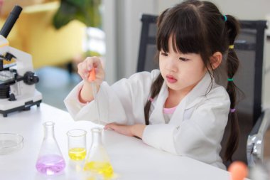 Laboratuvar önlüğü giymiş Asyalı küçük şirin kız öğrenciler deney tüpü bilim deneyleri yapıyorlar. Okulda kimya laboratuvarında. Eğitim araştırma ve geliştirme kavramı çocukları eğitiyor.