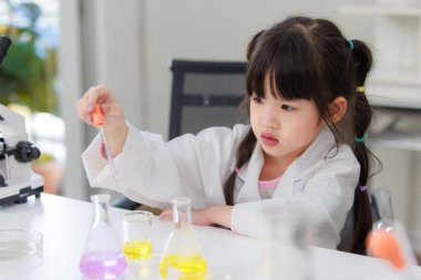Laboratuvar önlüğü giymiş Asyalı küçük şirin kız öğrenciler deney tüpü bilim deneyleri yapıyorlar. Okulda kimya laboratuvarında. Eğitim araştırma ve geliştirme kavramı çocukları eğitiyor.