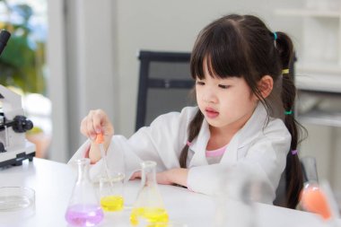 Laboratuvar önlüklü Asyalı küçük şirin kız öğrenciler, deney tüpü bilimi deneyleri yapmayı düşünüyorlar. Okulda kimya laboratuvarında. Eğitim araştırma ve geliştirme kavramı çocukları eğitiyor.