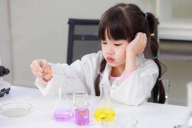 Laboratuvar önlüklü Asyalı küçük şirin kız öğrenciler, deney tüpü bilimi deneyleri yapmayı düşünüyorlar. Okulda kimya laboratuvarında. Eğitim araştırma ve geliştirme kavramı çocukları eğitiyor.