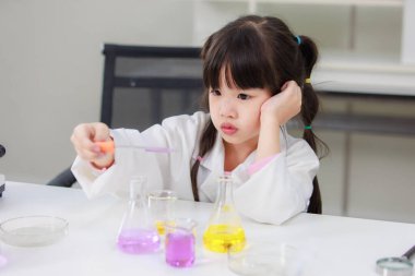Laboratuvar önlüklü Asyalı küçük şirin kız öğrenciler, deney tüpü bilimi deneyleri yapmayı düşünüyorlar. Okulda kimya laboratuvarında. Eğitim araştırma ve geliştirme kavramı çocukları eğitiyor.
