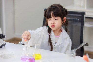 Laboratuvar önlüğü giymiş Asyalı küçük şirin kız öğrenciler deney tüpü bilim deneyleri yapıyorlar. Okulda kimya laboratuvarında. Eğitim araştırma ve geliştirme kavramı çocukları eğitiyor.