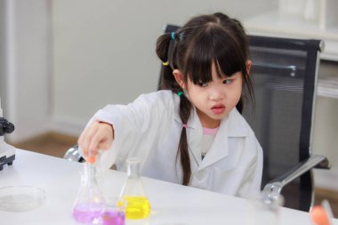 Laboratuvar önlüğü giymiş Asyalı küçük şirin kız öğrenciler deney tüpü bilim deneyleri yapıyorlar. Okulda kimya laboratuvarında. Eğitim araştırma ve geliştirme kavramı çocukları eğitiyor.