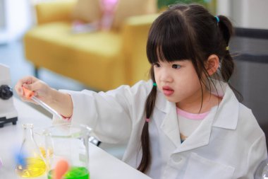 Laboratuvar önlüklü Asyalı küçük şirin kız öğrenciler, deney tüpü bilimi deneyleri yapmayı düşünüyorlar. Okulda kimya laboratuvarında. Eğitim araştırma ve geliştirme kavramı çocukları eğitiyor.