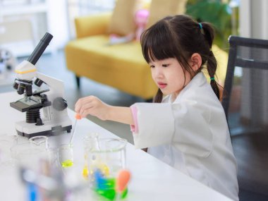 Laboratuvar önlüklü Asyalı küçük şirin kız öğrenciler, deney tüpü bilimi deneyleri yapmayı düşünüyorlar. Okulda kimya laboratuvarında. Eğitim araştırma ve geliştirme kavramı çocukları eğitiyor.