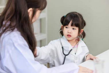 Asyalı kadın doktor ve neşeli küçük kız laboratuardaki doktor randevularına steteskop uyguluyorlar. Eğitim sağlık hizmetleri, tıp çocuklar için hastane konsepti çocuklar için öğrenme