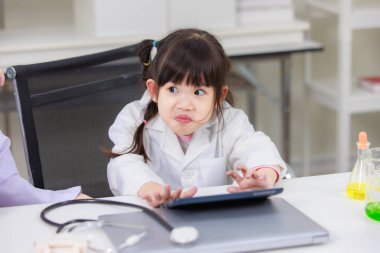 Laboratuvar önlüğü giymiş Asyalı küçük bir bilim adamı kimyasal laboratuvar çalışma odasında veri bilimi öğrenmek için tablet bilgisayar okuyor. Çocuklar için eğitim araştırması ve geliştirme kavramı.