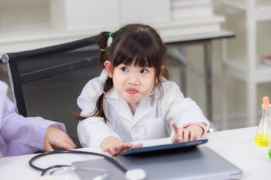 Laboratuvar önlüğü giymiş Asyalı küçük bir bilim adamı kimyasal laboratuvar çalışma odasında veri bilimi öğrenmek için tablet bilgisayar okuyor. Çocuklar için eğitim araştırması ve geliştirme kavramı.