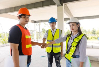 Asyalı erkek ve kadın inşaat şantiyesi çalışanları güvenlik teçhizatı ve sevinçli istifleme elleri profesyonel ortamlardaki olumlu başarıları motive etmek için takım çalışması veya birlik için jestler gösteriyor..