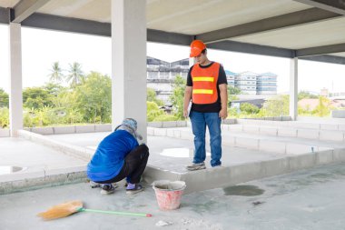Asyalı inşaat mühendisi, güvenlik önlüğü takıyor, çelik yelek giyiyor, görüş mesafesi yüksek, işçilerin inşaat alanında veya inşaat geliştirme konseptinde çalışmalarını denetliyor..