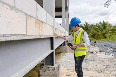 Asyalı inşaat mühendisi inşaat mühendisi ustabaşı güvenlik donanımı ve miğfer taşıyan miğfer taşıma tablet planlama projesi ve mimar geliştirme çalışmalarını denetliyor.