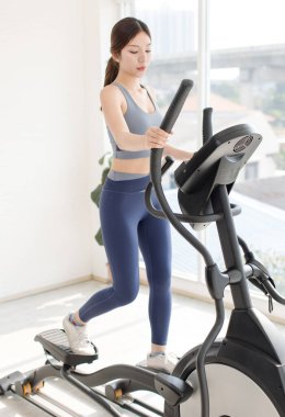 Asyalı, güzel, neşeli, neşeli, aktif bir kız spor giyim, sabit bisiklet hareketleri spor salonunda hız enerjisi eğitimi evde ya da oturma odasında sağlıklı bir yaşam tarzı.