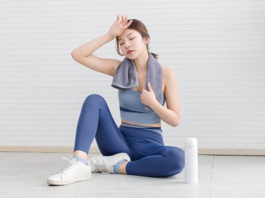 Asya 'lı genç ve çekici bir kadın spor kıyafetlerini giymiş yerde oturuyor, kadın spor yaptıktan sonra rahatlıyor oturma odasındaki kameraya gülümsüyor, sağlık hizmetleri yaşam tarzına bakıyor..