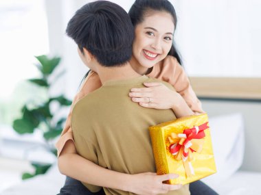 Genç Asyalı mutlu çiftin portresi süpriz hediye anlarını sever. Erkek kucaklaşması, sevgililer gününde sevgililer gününde yatak odasında sevgilisine hediye paketi verir. Romantik bir sürpriz..