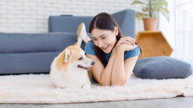 Neşeli Asyalı genç güzel kadın sevimli Galli Corgi köpeğiyle mutlu bir gülümseme ile hayvanlarla poz verirken ev konsepti yaşam tarzının oturma odasında halı üzerinde uzanırken evcil hayvan en iyi arkadaşının keyfini çıkar..