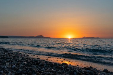 Bu ıslak çakıl taşları Yunanistan 'ın Girit kentindeki Rethymno yakınlarında güzel bir günbatımında kumsalda parlıyor.