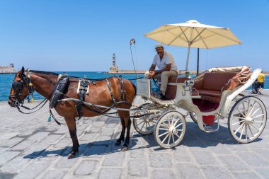 Bir arabacı, Yunanistan 'ın Girit kentindeki eski Chania kasabasında yeni yolcular için güzel at arabasıyla bekliyor.