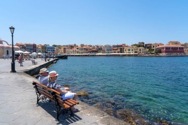 Yunanistan 'ın Girit kentindeki eski Chania kentinde güzel bir liman manzarası olan bir bankta oturan insanlar