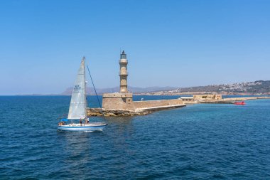Bir yelkenli gemisi eski deniz fenerini geçiyor ve Girit, Chania limanına doğru yelken açıyor.