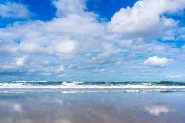 Dalgaların üzerindeki güzel bulutlar, Vlieland 'in kuzey tarafındaki kumsaldaki geri çekilen suya yansıyor.