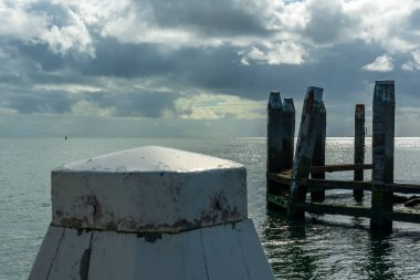 Vlieland limanının demirleme noktalarına bakın ve arka planda güneş ağır bulutların arasından doğuyor ve Wadden Denizi 2 'nin suyuna yansıyor.