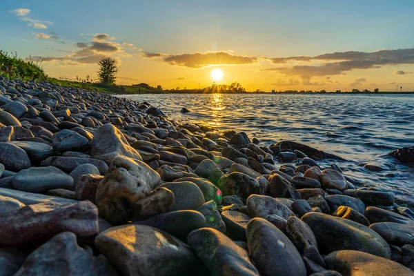 The setting sun shines on the water and on the large pebbles along the bank of the river De Lek near Beusichem, the Netherlands