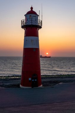 Gün batımında Westkapelle yakınlarındaki Deniz fenerinden bir kargo gemisi geçiyor.
