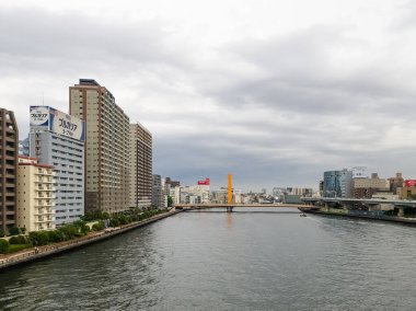 Sumida Nehri ile Tokyo şehir manzarası, modern binalar ve bulutlu gökyüzü altında köprü manzarası