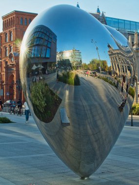 Lodz çarpıtması. Lodz, Polonya - 21 Eylül 2023 Lodz 'daki çarpık binalar, hayır kurumlarına adanmış şehir heykeline yansıdı..