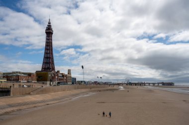 BLACKPOOL MAY 1 2023: Blackpool's World Famous Tower and tourists and day trippers on the beach in front of it as seen from the North Pier. clipart