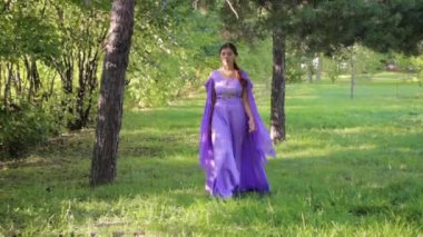 Ortaçağ elbisesi içinde genç ve çekici bir kadın bir yaz parkında yürüyor..