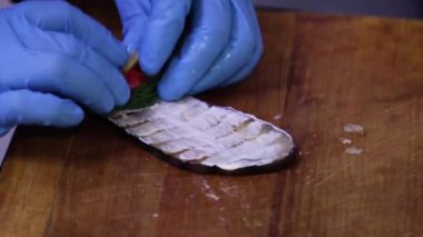 Şefin ellerinin mavi eldivenli yakın çekimi patlıcan rulosunu mayonez ve domatesle kaplıyor..