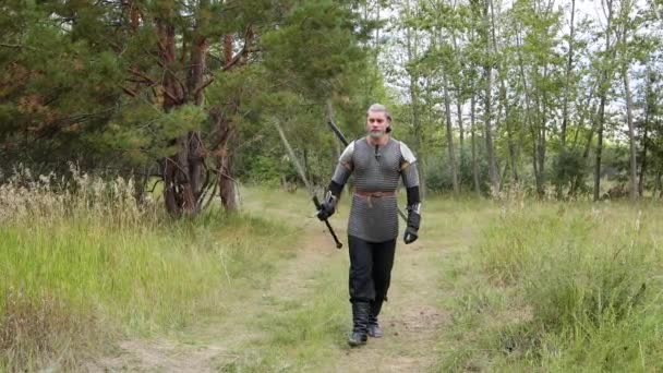 一位中世纪的战士 头发灰白 戴着带肩垫的链子 手里拿着一把双手的剑 小心翼翼地走着 蹲在森林里 中世纪的猎手 — 图库视频影像