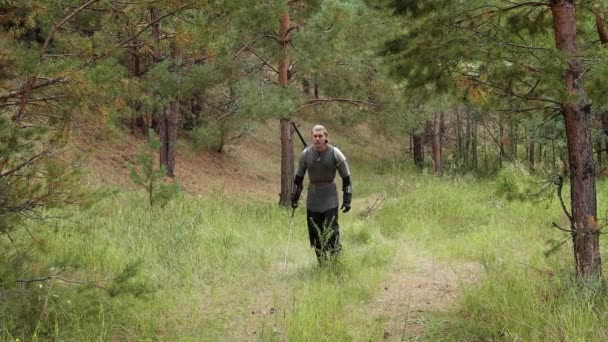 一位中世纪的战士 头发灰白 戴着带肩垫的链子 手里拿着一把双手的剑 小心翼翼地走着 蹲在森林里 中世纪的猎手 — 图库视频影像