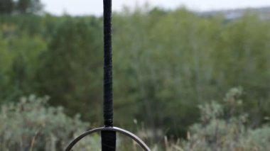 Pürüzsüz kamera hareketi, seçici odaklanma, yerde sıkışmış iki elli bir kılıç bir tarlanın, ormanın ve gökyüzünün arka planında. Kayıp, unutulmuş kılıç, düşmüş savaşçı.