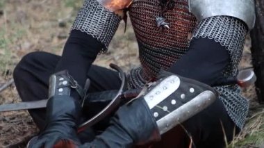 Bir ortaçağ savaşçısının portresi, gri saçlı, yüzünde zincirli bir yara izi omuzluk ve elinde iki elli bir kılıç ile bir ağacın yanında oturuyor. Orta Çağ Cadısı