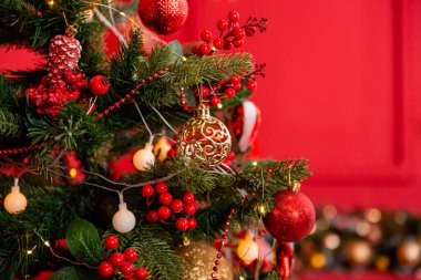 Close-up of a Christmas tree with decorations on a background of a red wall with a bokeh of yellow garlands.