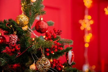 Close-up of a Christmas tree with decorations on a background of a red wall with a bokeh of yellow garlands.