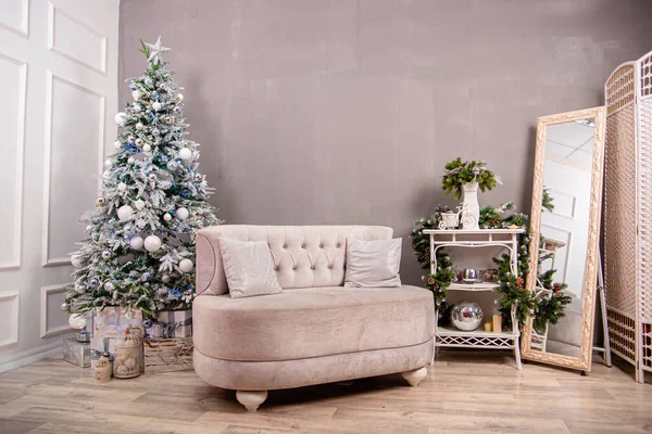 White sofa against the backdrop of a Christmas tree and a gray and white wall. New years background.