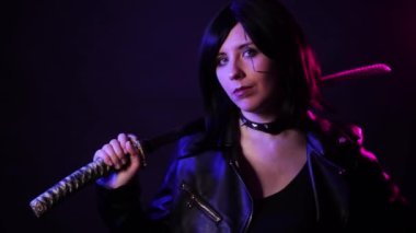 Siyah deri ceketli, elinde katana olan, mavi ve mor arka fonda izole bir şekilde poz veren kısa saçlı genç bir kadının portresi, siber punk konsepti..