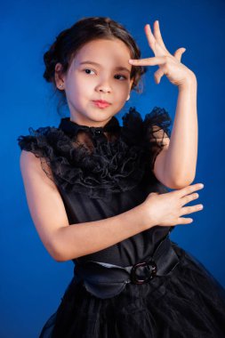 Kafasında örgülü saç stili olan siyah elbiseli küçük bir kızın portresi, koyu bir arka planda, mavi arka planda izole edilmiş.. 