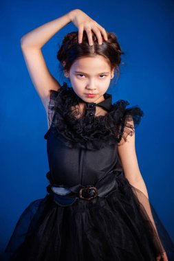 Kafasında örgülü saç stili olan siyah elbiseli küçük bir kızın portresi, koyu bir arka planda, mavi arka planda izole edilmiş.. 