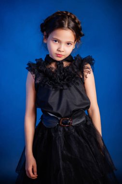 Kafasında örgülü saç stili olan siyah elbiseli küçük bir kızın portresi, koyu bir arka planda, mavi arka planda izole edilmiş.. 