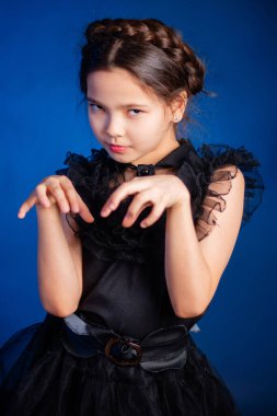 Kafasında örgülü saç stili olan siyah elbiseli küçük bir kızın portresi, koyu bir arka planda, mavi arka planda izole edilmiş.. 