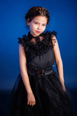 Kafasında örgülü saç stili olan siyah elbiseli küçük bir kızın portresi, koyu bir arka planda, mavi arka planda izole edilmiş.. 